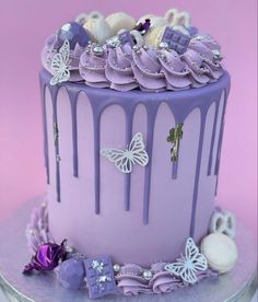 there is a purple cake with white butterflies on the top and blue icing dripping down the side