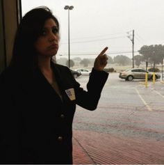 a woman pointing at something in front of a window with cars parked on the street behind her