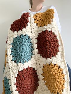 a woman is holding up a crocheted blanket