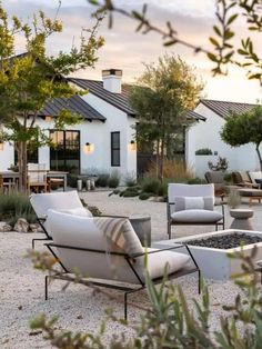 an outdoor living area with chairs, tables and fire pit in front of a white house