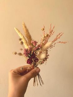 a hand holding a flower arrangement in front of a wall