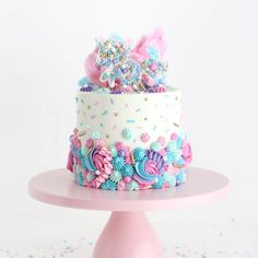 a multi layer cake with sprinkles and flowers on a pink stand against a white background