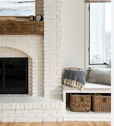 a white brick fireplace in a living room with two baskets under the mantle and a painting on the wall