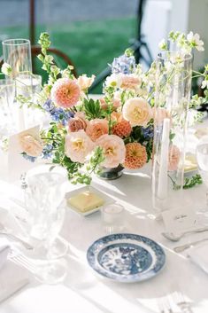 an arrangement of flowers on a table with plates and utensils in the foreground