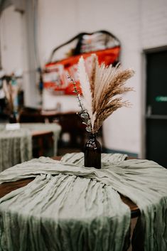 a vase with some dry grass in it on top of a round table cloth covered table