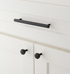 a white cabinet with black handles and knobs