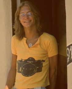 a man with glasses and a camera on his shirt is standing in front of a door