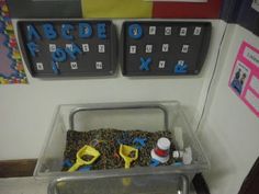 a plastic container with scissors and other items in it sitting on the floor next to a bulletin board