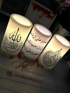 three lit candles with arabic writing on them