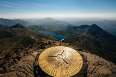 a clock sitting on top of a rock in the middle of a mountain range next to a lake