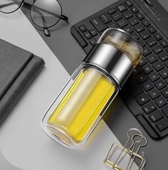 a glass bottle filled with yellow liquid sitting on top of a desk next to a keyboard