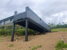 a large metal structure sitting on top of a dirt field next to a building and trees