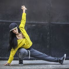 a woman in yellow shirt and black hat doing a dance move on the street with her hands up