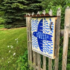 a wooden fence with a blue bird painted on the top and bottom, in front of some trees