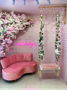 a pink couch and chair in front of a brick wall with flowers hanging from it