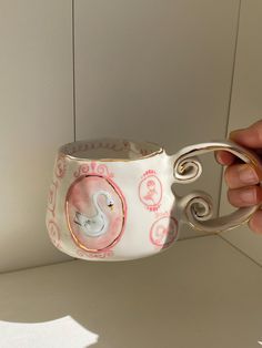 a hand holding a white and pink cup with a swan on the inside of it