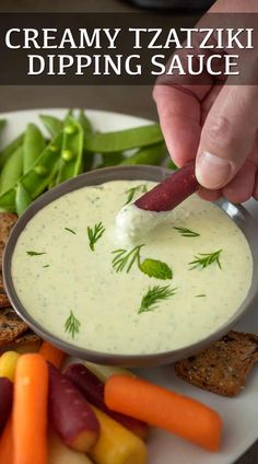 a person dipping dip into a bowl of dip surrounded by veggies and crackers