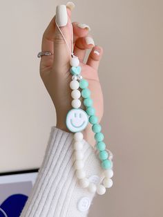 a woman holding up a bracelet with beads and charms on it's wrist while wearing a white sweater