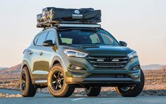 the front end of a silver suv with luggage on top and mountains in the background