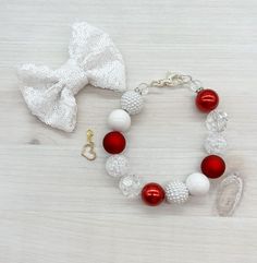 a red and white beaded bracelet with a bow tie on a wooden table next to it