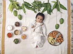 a baby is laying on a blanket with food around him and there are green leaves hanging from the branches