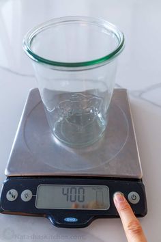 a person pointing at a glass on top of a scale