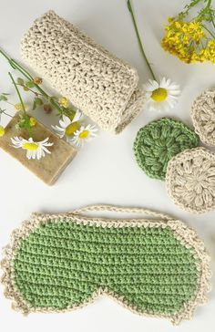 crocheted purses and coasters are laid out on a white surface next to flowers