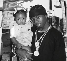 a black and white photo of a woman holding a baby in her arms with another person standing behind her