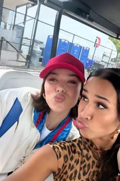 two young women are taking a selfie in the back of a car, one is sticking her tongue out