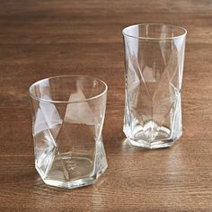 two clear glass tumblers sitting on top of a wooden table next to each other