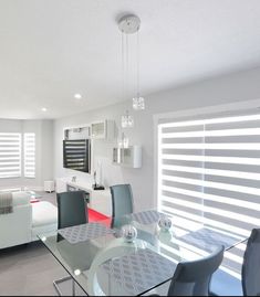 a glass dining table and chairs in a room with blinds on the window sill