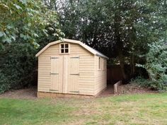 a wooden shed sitting in the middle of a lush green field next to some trees