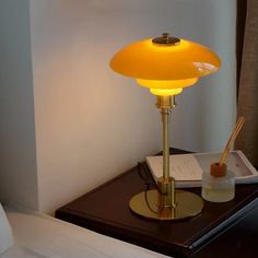 a yellow lamp sitting on top of a wooden table next to a book and pen