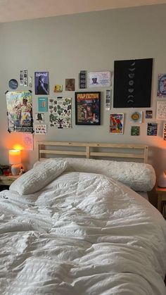 an unmade bed with white comforter and posters on the wall