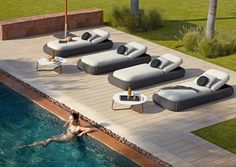 a woman swimming in a pool next to lounge chairs