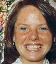 a woman with freckled hair and blue eyes smiles at the camera while wearing a wedding dress