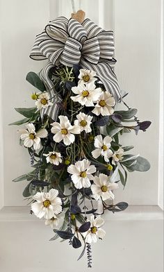 a wreath with white flowers and green leaves hanging from the front door, decorated with a bow