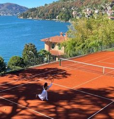 two people on a tennis court with trees and water in the background