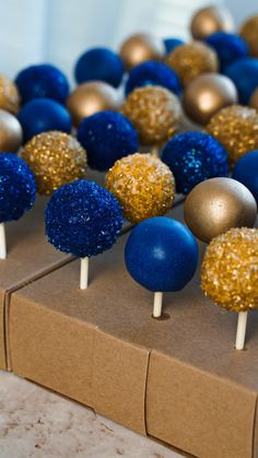 blue and gold cake pops are sitting on a brown box with silver and gold decorations