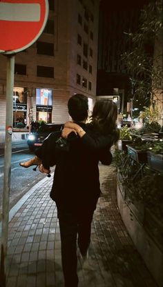 a man carrying a woman on his back while walking down the street at night time