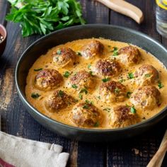 a pan filled with meatballs and sauce on top of a wooden table next to some parsley