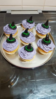 cupcakes with purple frosting and green witches hats on top are sitting on a plate