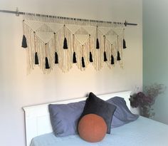 a white bed topped with lots of pillows and tassels hanging from the wall