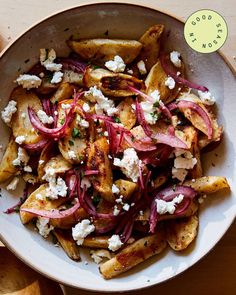 a bowl filled with potatoes and onions on top of a wooden table next to utensils