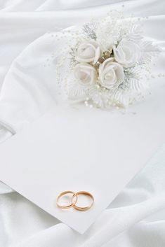 two gold wedding rings sitting on top of a white sheet next to a bouquet of flowers