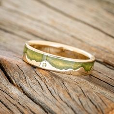 a gold ring with green and white designs sitting on top of a piece of wood