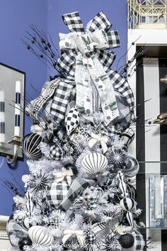 a white christmas tree with black and white ornaments on it's top, in front of a blue wall