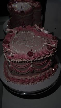 two tiered cakes with pink frosting and decorations on them, one has a candle in the middle