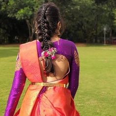 a woman in an orange and purple sari with braids on her head walking across a field