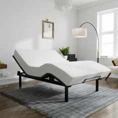 a white bed sitting on top of a wooden floor next to a chair and lamp